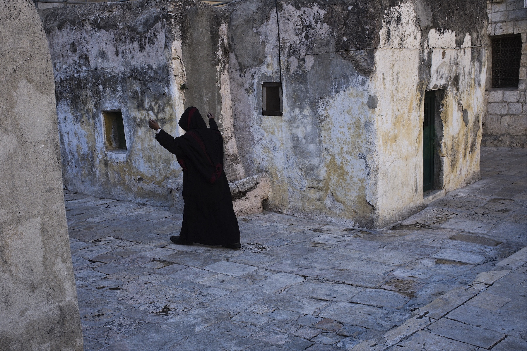 A hooded Christian priest walks with his hands up in the courtyard of a church in Jerusalem during Holy Week